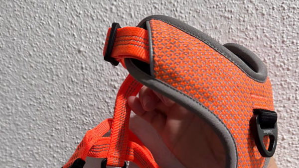 Mão segurando peitoral laranja de tela respirável